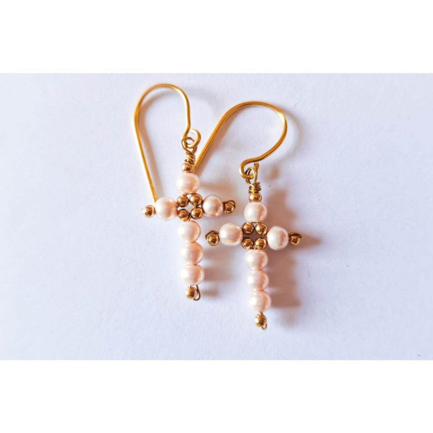 Pair of gold cross-shaped earrings with pink beads on a white background